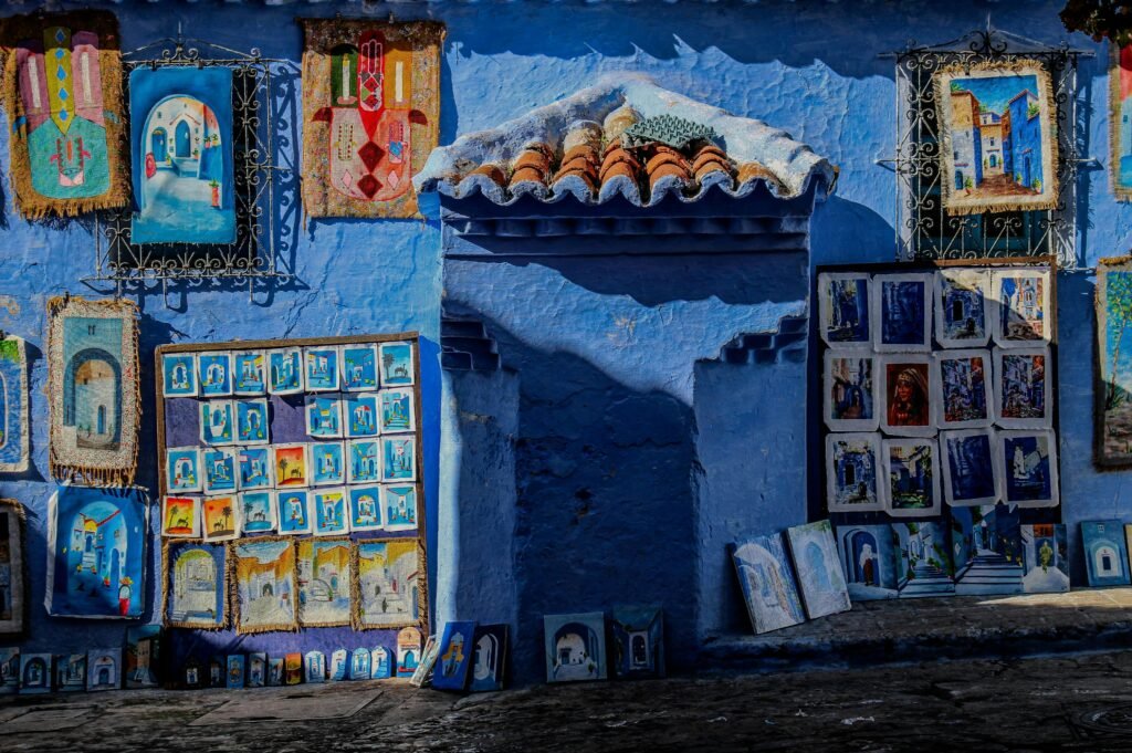 Colorful artwork displayed on a blue wall in Chefchaouen, Morocco, capturing local culture.