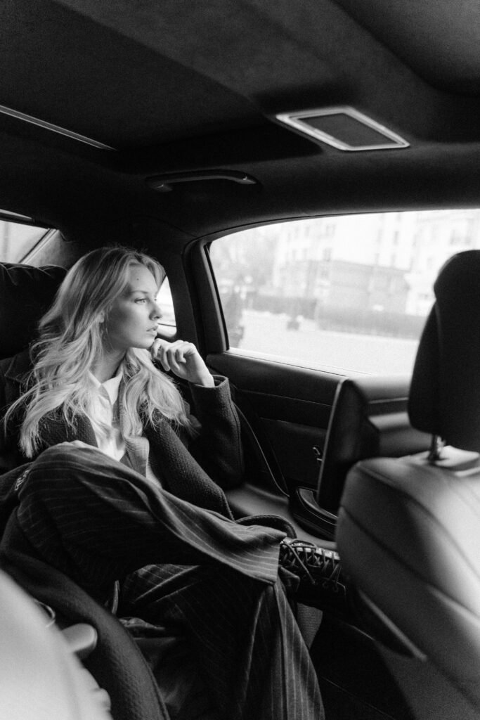 Black and white image of a thoughtful businesswoman sitting in a luxury car, exuding professionalism.