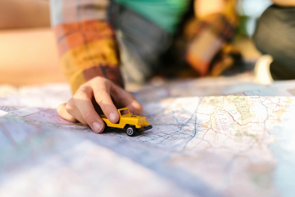 Close-up of a hand with a yellow toy car on a map, symbolizing travel planning.